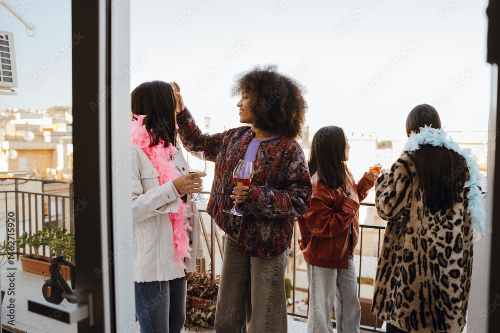 Obraz premium A group of four female friends hold glasses while standing on a balcony