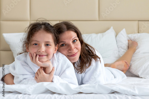 Mom and daughter in white coats on a large bed in a 5-star hotel