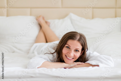 A young woman in a white bathrobe lies on a large bed in a hotel
