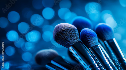 Professional makeup brushes arranged artistically against vibrant blue background, creating visually striking effect. soft bristles and shiny handles reflect light beautifully, evoking sense