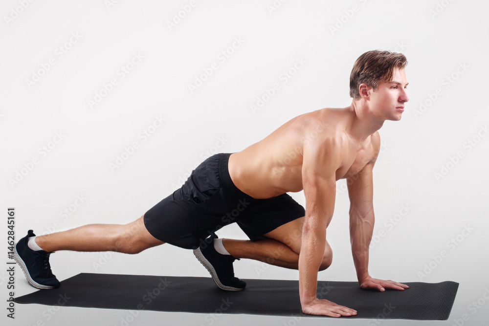 Obraz premium Healthy lifestyle and sports concept. Strong young man with naked chest exercising on yoga mat over light studio background. Motivated millennial sportsman doing pilates, full length