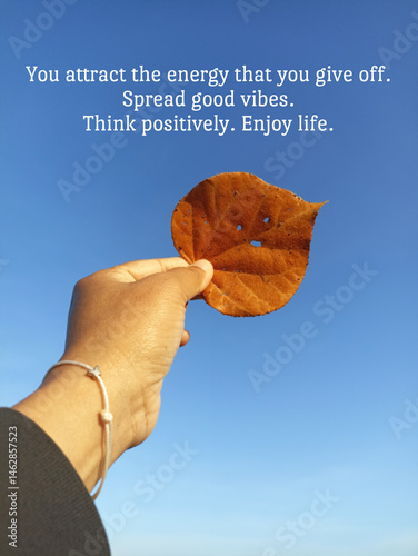 Inspirational motivational quote - You attract the energy that you give off. Spread good vibes. Think positively. Enjoy life. With person holding dry leaf in hand against blue summer sky background.