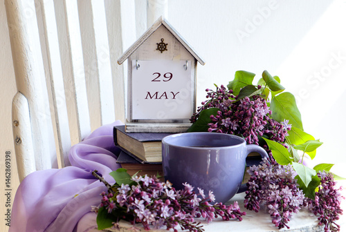 Calendar for May 29: numbers 29, word May in English on a decorative calendar, cup of tea, lilac branches on a chair photo