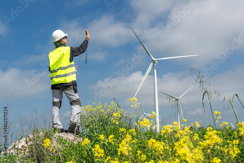 Engineer measuring wind turbine efficiency with anemometer in field of yellow flowers