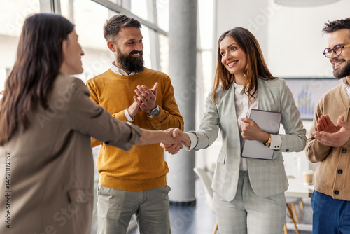 Photos Two successful businesswomen shaking hands and closing deal and partnership while businessmen applauding them