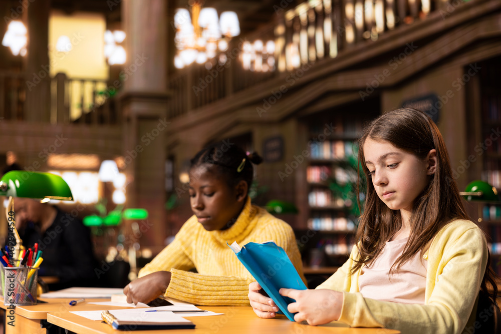 Diverse teenagers engrossed in reading books at the school library, focusing on literature and knowledge while they are preparing for their academic lessons and school assignments.