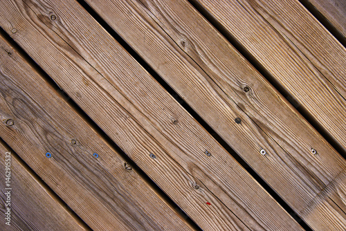 Top view of wooden floor texture. Diagonal wooden planks with grain, screw marks, nail heads typical for boardwalk or pier flooring
