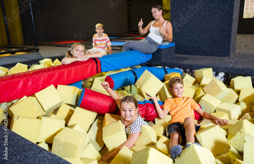 Cheerful excited tween children having fun in pool with soft yellow foam cubes, playing in modern indoor inflatable amusement park