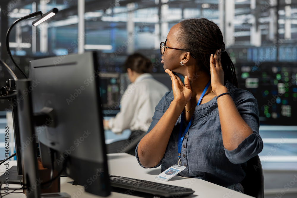 Fatigued data center technician stretching neck while inspecting gear, doing maintenance tasks. Exhausted server farm employee relaxing tensed muscle joints taking break from conducting system checks