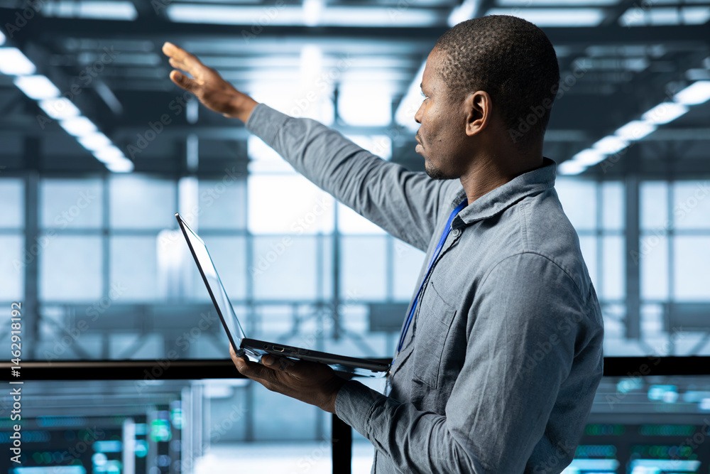 Technician holding laptop, looking around data center, managing server virtualization, finetuning network protocols, verifying high availability configurations, enforcing advanced security measures