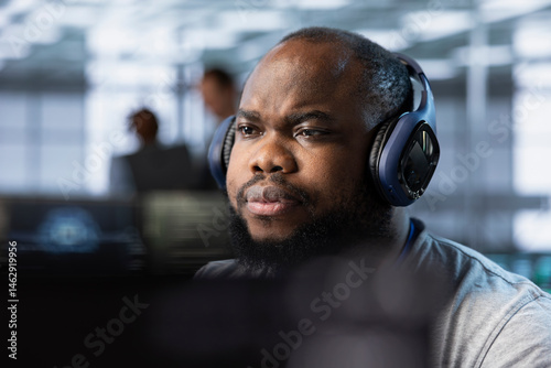 Obraz na płótnie African american admin wearing headphones implementing cybersecurity measures to protect data center. Server hub worker listening music, analyzing metrics to enhance operational effectiveness w salonie