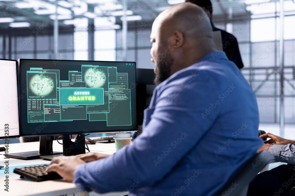 Access granted notification on monitor received by man reconfiguring server hub, optimizing it. African american data center IT expert using PC to successfully eliminate all errors