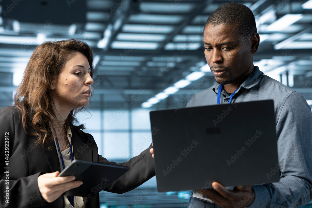 System administrators using laptop in data center, managing server virtualization. IT specialists using notebook in server room, sustaining long term infrastructure reliability