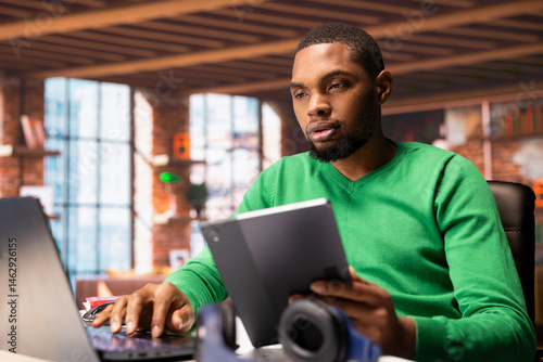 Remote worker using laptop and tablet in home office to write emails. Freelancer using digital devices, composing documents in order to deliver finalized project paperwork
