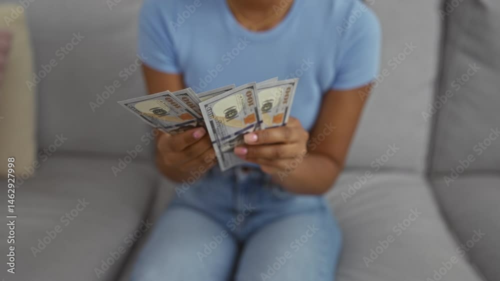Woman counting dollars indoors in a casual home setting showing young adult hands holding american money seated in a living room