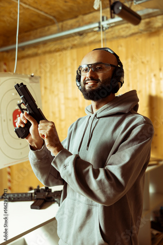 Obraz na płótnie Portrait of happy Arab man in shooting range cocking handgun, setting mechanism up for firing. Cheerful Middle Eastern person pulling back pistol hammer during training session, preparing to shoot w salonie