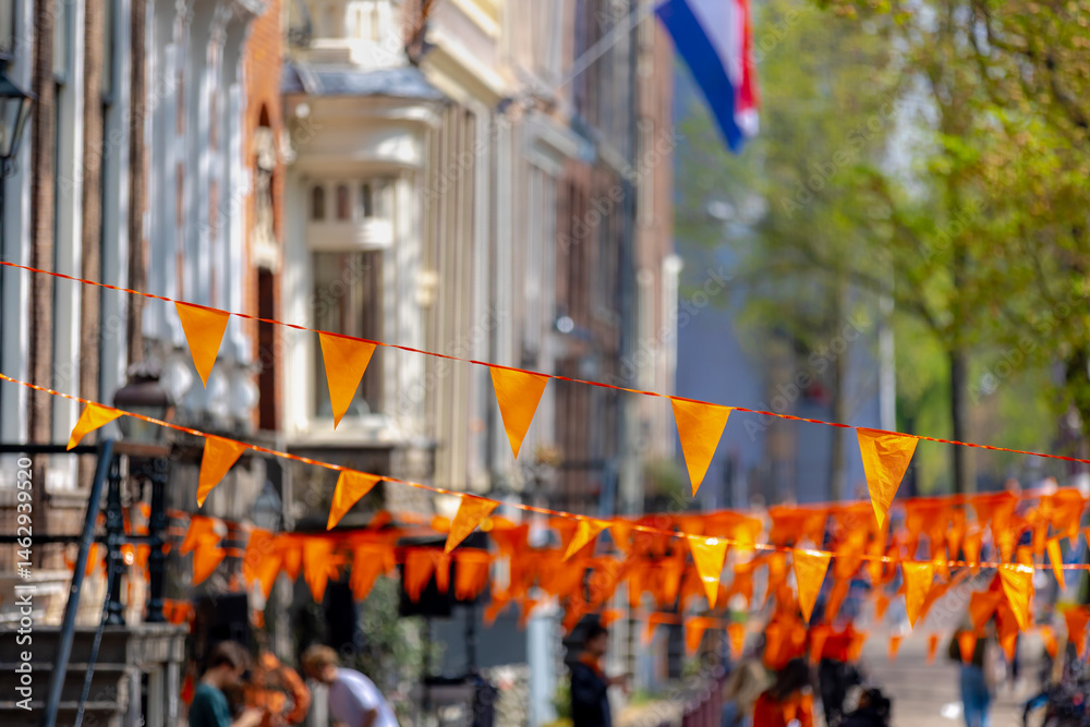 Colourful of King’s Day (in Dutch: Koningsdag) Selective focus of pennant orange flags hanging outside building with blurred peoples walking on street as background, National holiday in Netherlands.
