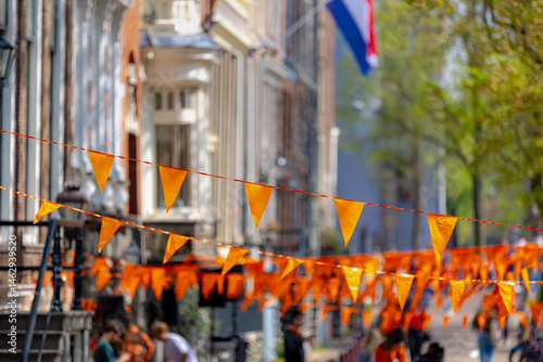 Obraz na płótnie Colourful of King’s Day (in Dutch: Koningsdag) Selective focus of pennant orange flags hanging outside building with blurred peoples walking on street as background, National holiday in Netherlands. w salonie