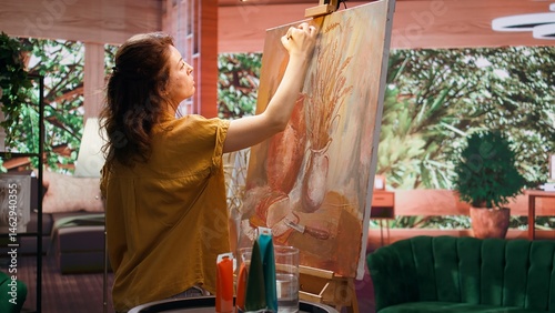 Obraz na płótnie Skilled painter stands before a canvas painting a watercolor rustic artwork. Artist showing her skill and brush technique as she mixes dyes, creating a multicolored masterpiece. Camera B. w salonie