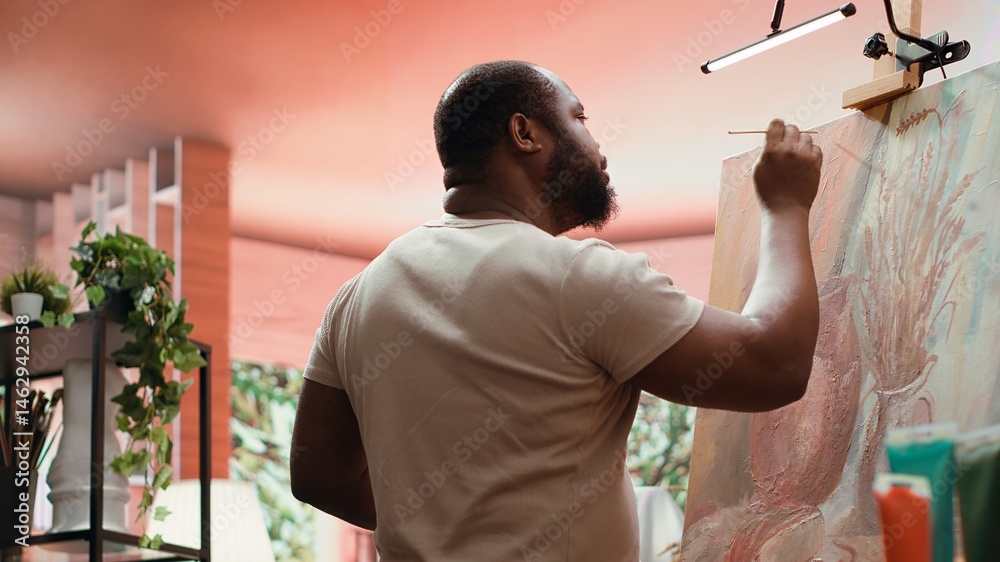 African american artist using his skill to paint a new creation in art studio, using innovative painting technique for his masterpiece. Young contemporary painter working on an artwork. Camera A.