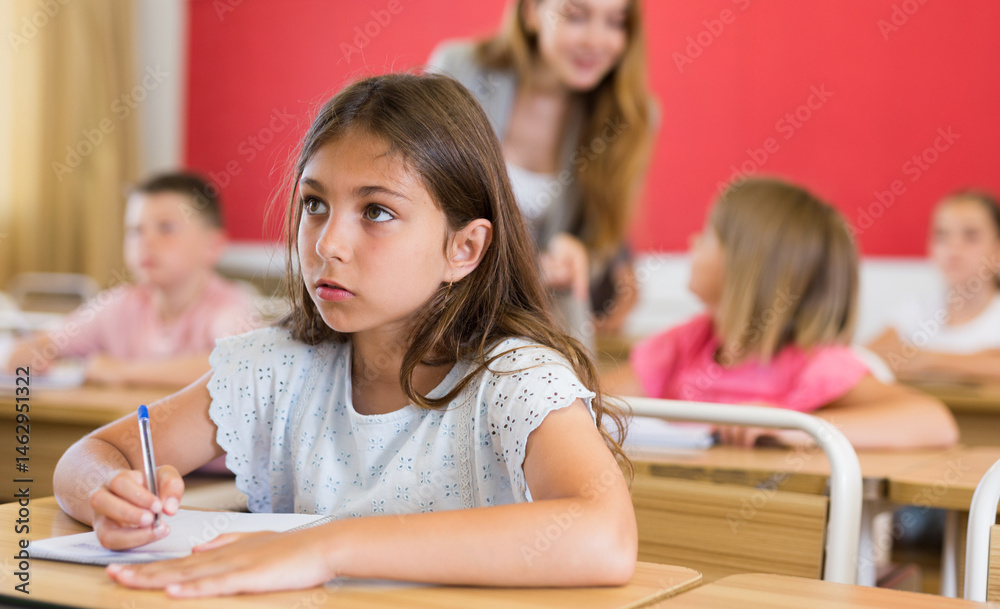 Fototapeta premium Diligent elementary school student tween girl studying with classmates, making notes of teacher lecture