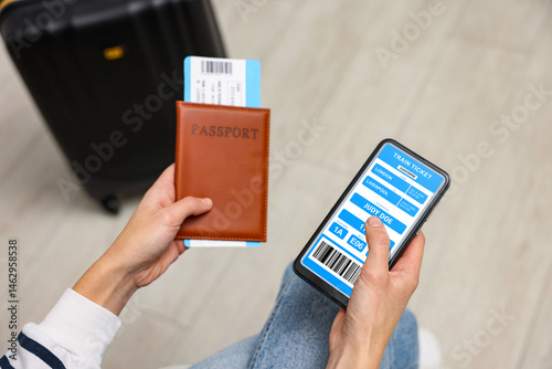 Tourist holding mobile phone with e-ticket for train and passport indoors, closeup