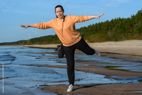 Woman balancing on one leg on a wild sandy beach by the Baltic Sea.