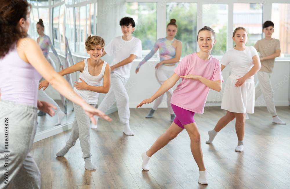 Naklejka premium Young girls and boys repeat the movements of dance teacher, training in a spacious studio