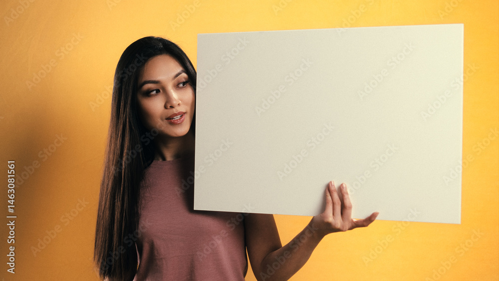 Smiling young woman holding a blank white board with copy space on a vibrant yellow background, studio shot Smiling young woman holding a blank white board with copy space on a vibrant yellow background, studio shot