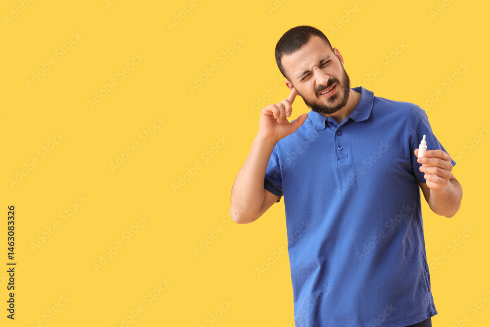 Young man with drops suffering from ear pain on yellow background Young man with drops suffering from ear pain on yellow background