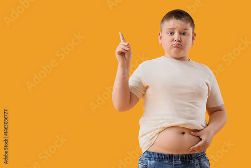 Sad overweight boy pointing at something on yellow background. Diet concept