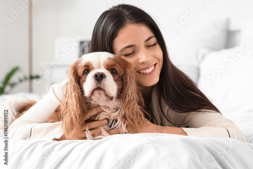Obraz na plátně Beautiful young woman with cute cavalier King Charles spaniel lying on bed at ho