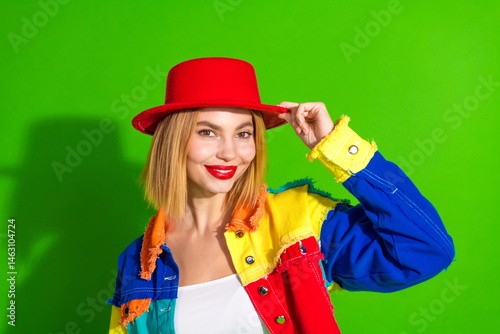 Εκτύπωση καμβά Smiling young woman in vibrant outfit and red hat against a green background sho