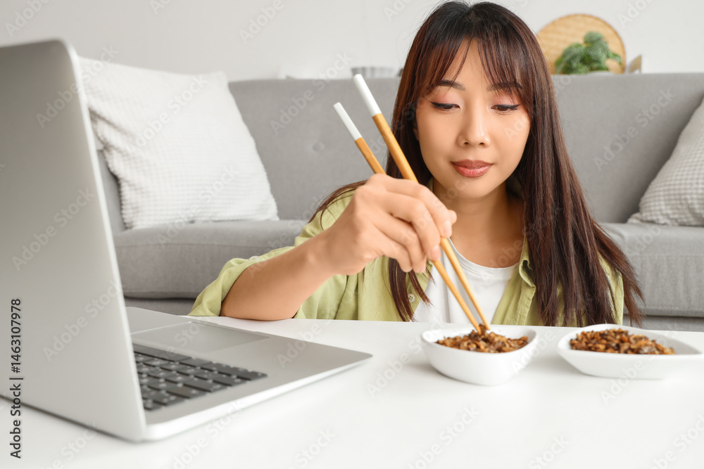 Beautiful Asian woman with chopsticks eating fried insects and laptop on table at home Beautiful Asian woman with chopsticks eating fried insects and laptop on table at home
