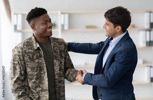 Obraz na plátně Cheerful guy in blue suit shaking happy young black military man hand, psychologist and soldier celebrating successful therapy, clinic interior