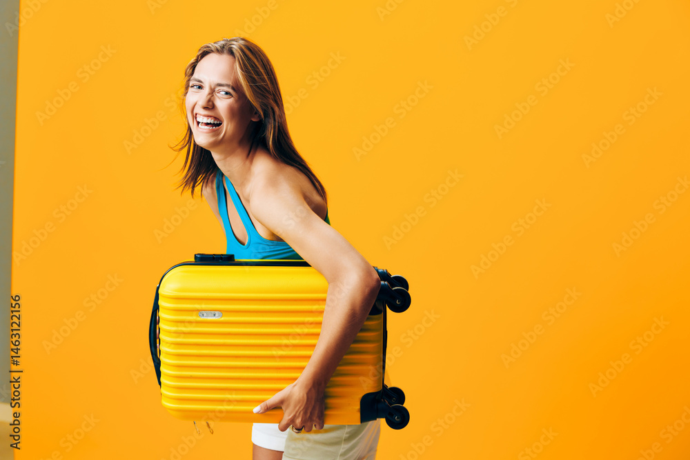© SHOTPRIME STUDIO - Cheerful woman holding a vibrant yellow suitcase standing against a bold orange wall with a joyful expression