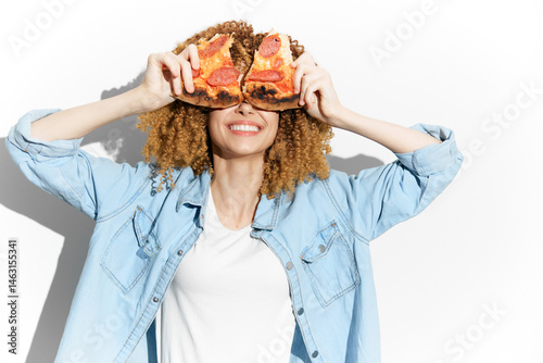 Obraz na płótnie Smiling woman with curly hair holding pizza, wearing a denim shirt in a bright setting, representing joy and fun in food enjoyment w salonie