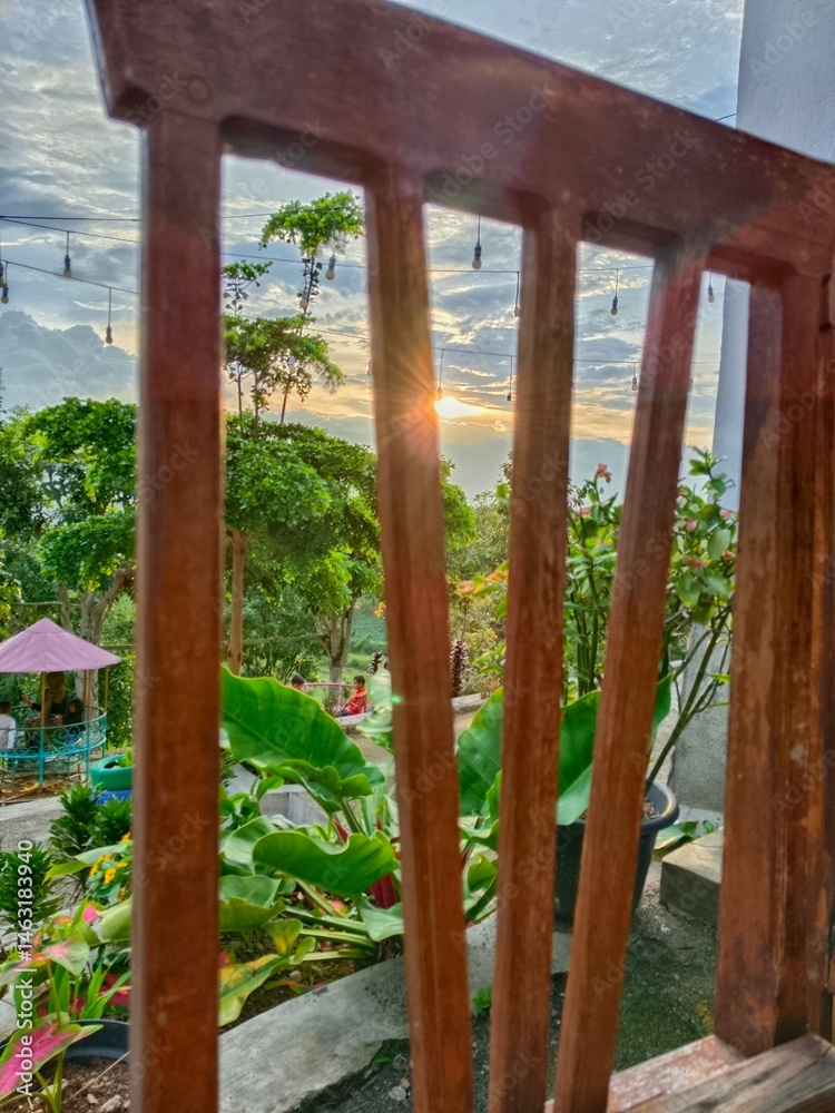 Fototapeta premium Viewing Garden Sunset Through Wooden Railing Greenery and Sky