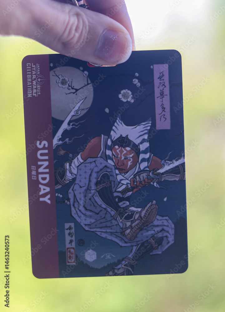 Fototapeta premium Tokyo, Japan - May 8, 2025 - Caucasian hand holding an entry badge for Sunday for the Star Wars Celebration 2025 featuring an artwork of the character Ahsoka Tano