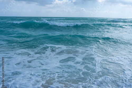 Obraz na płótnie Turquoise sea water wave motion. Summer beach. Calm sea. Luxury seaside resort. Bright sky and waves on beach. Beautiful foamy shoreline. Sea background. Blue ocean. Sandy ocean beach. Sea waves. w salonie