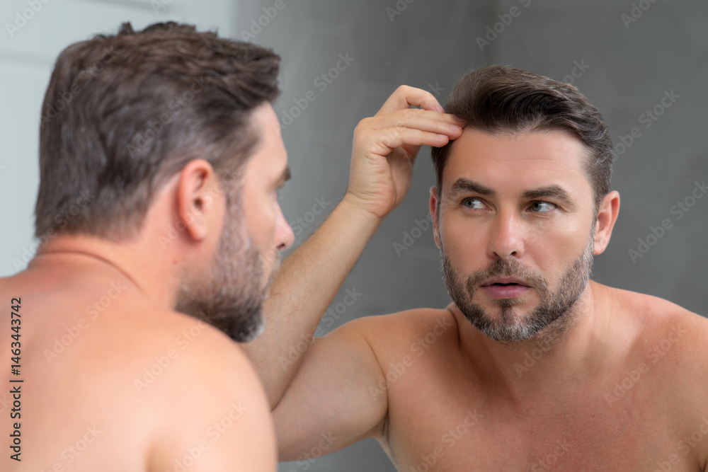 Obraz premium Close-up male wrinkles. Portrait of brunet man touching skin wrinkles. Middle aged man with touch wrinkles in front of the mirror. Aged skin. Man 40s cosmetic, skin treatment. Male face with wrinkles.