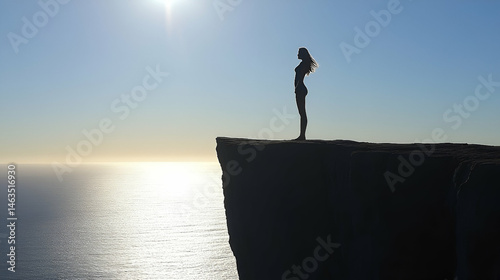 Silhouette of a Woman Standing on a Cliff overlooking the Ocean at Sunset
