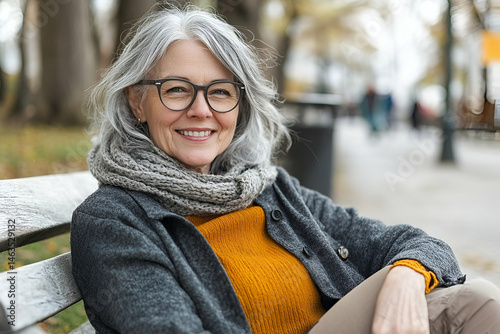 Smiling Senior Woman Sitting on a Park Bench in Autumn