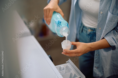 Foto Close up of woman using fabric softener while washing clothing in laundry room