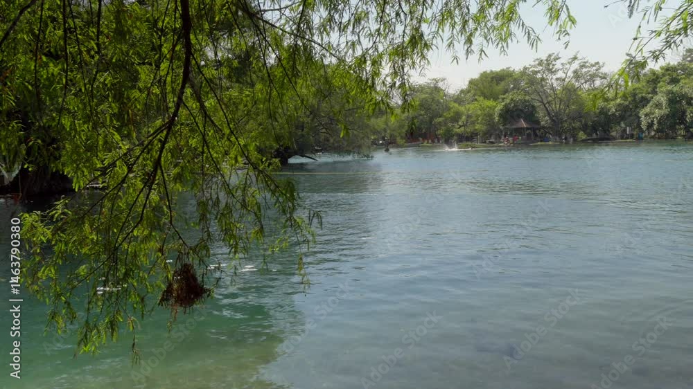 Crystal clear waters of Colón Lakes, La Trinitaria, Chiapas, Mexico, with indistinct visitors swimming in the distance. Framed by a natural tree vignette. Perfect for nature and travel content