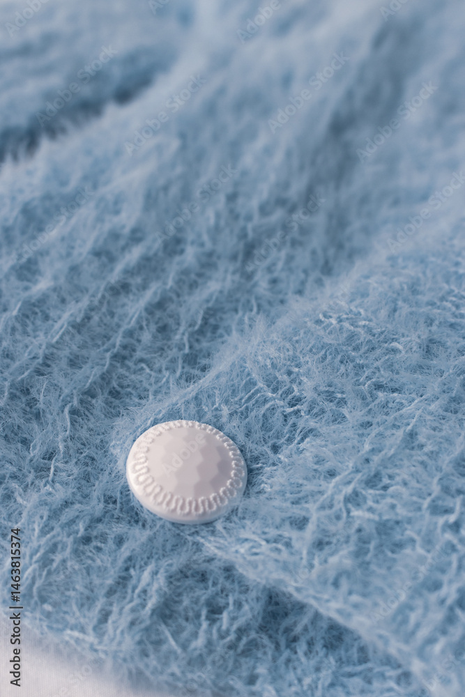 Blue knitted cardigan with white button on white background. Soft blue knitted sweater in details. Knitting pattern background. Summer knitted fashion. Cozy hobby. Craft product concept.
