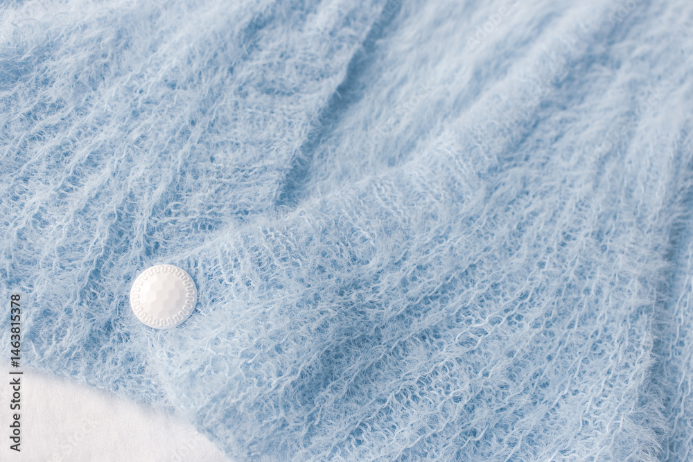 Blue knitted cardigan with white button on white background. Soft blue knitted sweater in details. Knitting pattern background. Summer knitted fashion. Cozy hobby. Craft product concept.