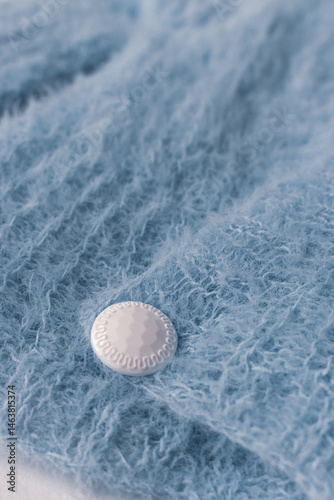 Obraz na płótnie Blue knitted cardigan with white button on white background. Soft blue knitted sweater in details. Knitting pattern background. Summer knitted fashion. Cozy hobby. Craft product concept. w salonie