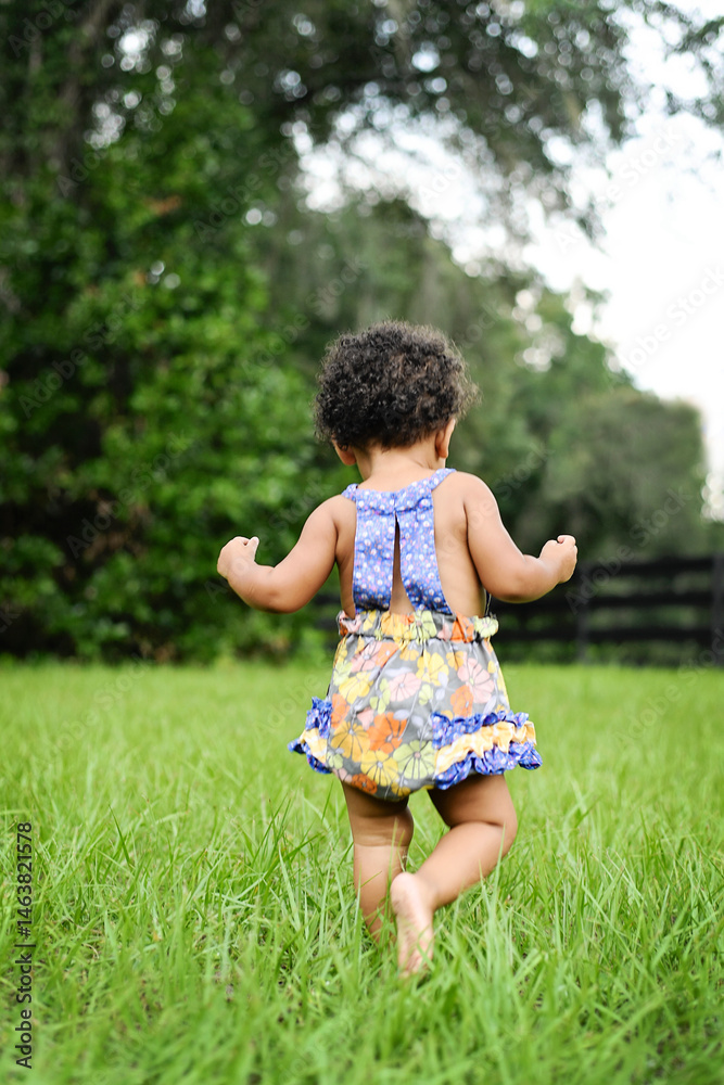 Toddler in floral dress explores a lush green garden. Toddler in floral dress explores a lush green garden.