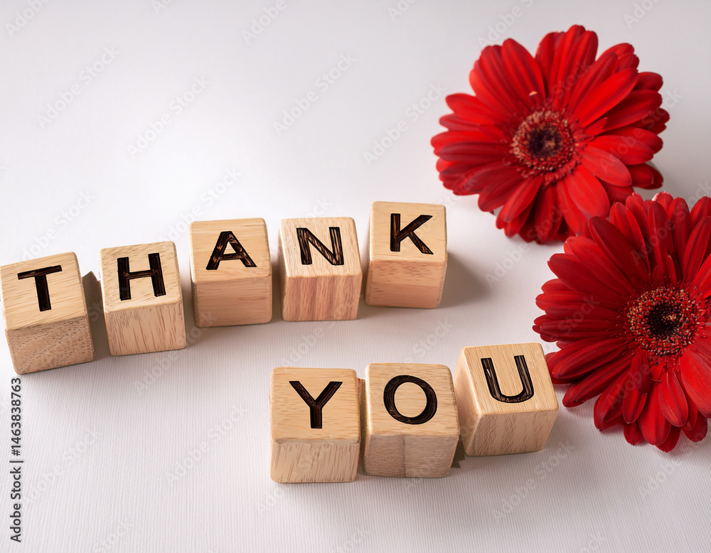 The word THANK YOU written in wooden cubes on a white background with few flowers